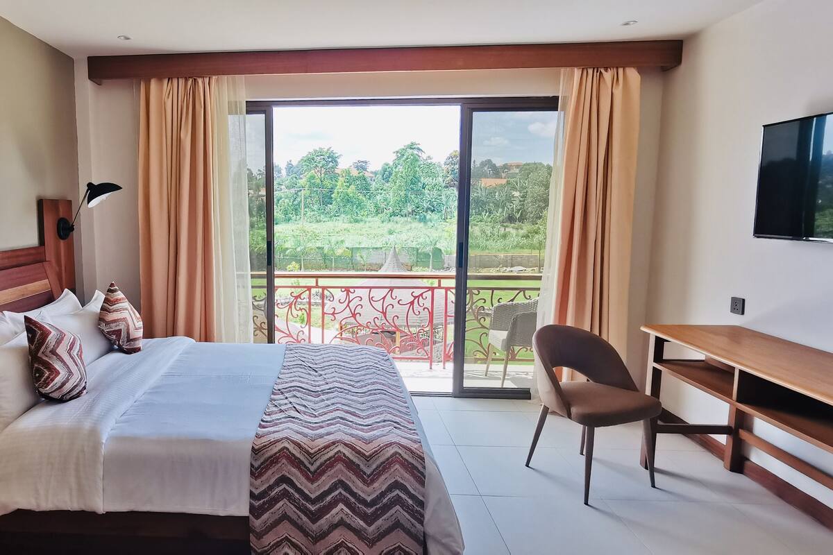 A hotel room with a bed, desk, chair, and a balcony with a view.