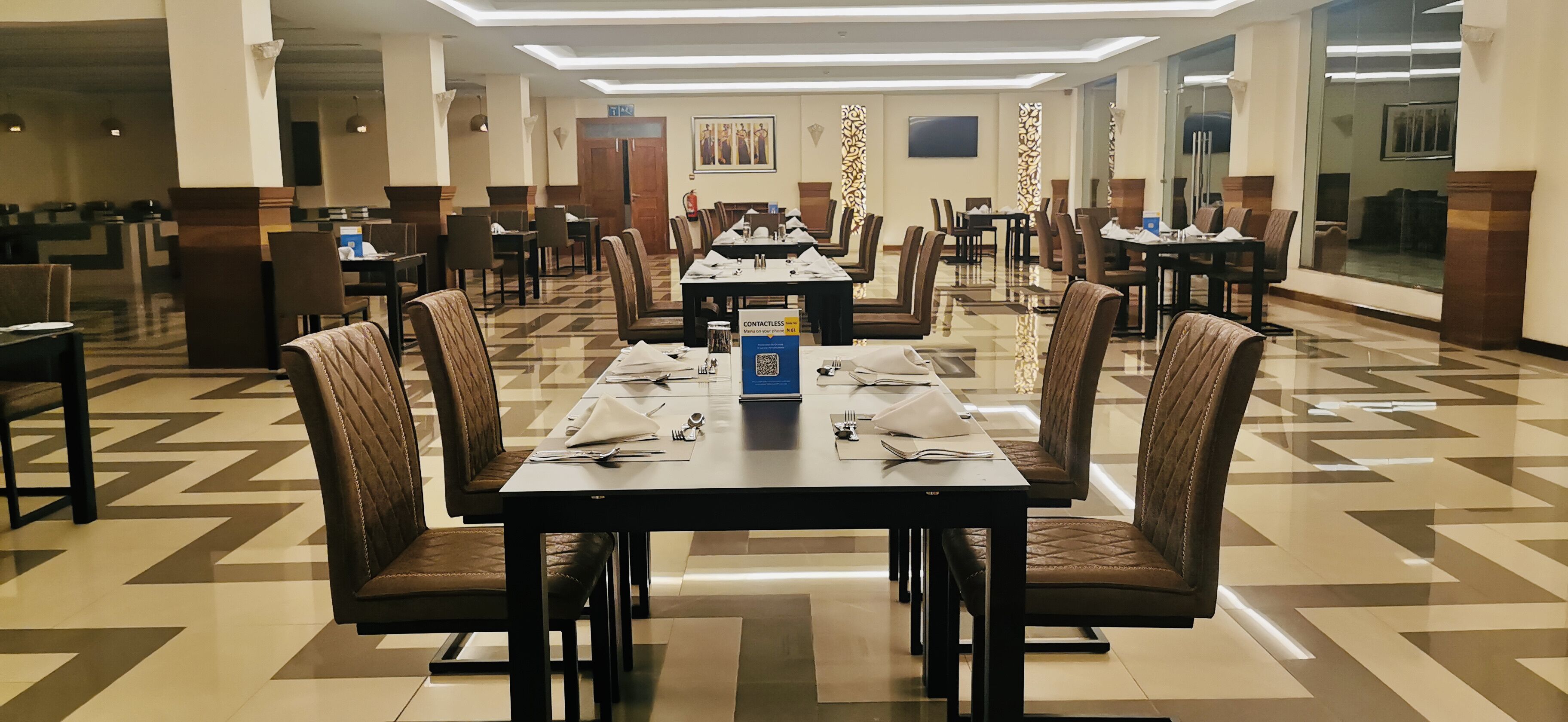 A hotel dining area with multiple tables set for service, equipped with chairs and table settings.