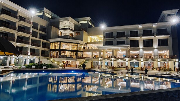A multi-story hotel with a swimming pool, outdoor seating, and a well-lit facade. - Kampala Nile Resort (Seeta)