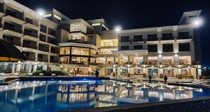 Un hôtel à plusieurs étages doté d’une piscine, d’un espace extérieur aménagé et d’une façade bien éclairée.