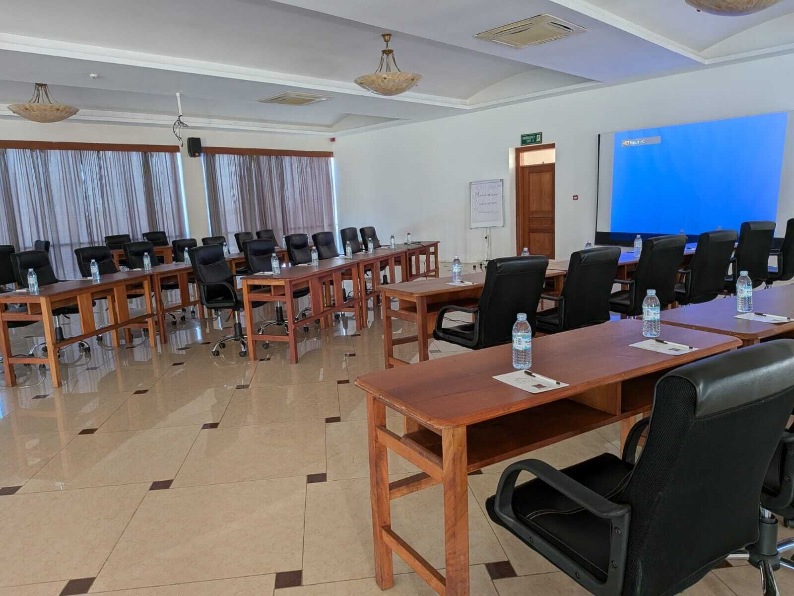 A conference room with multiple tables and chairs, a whiteboard, and a blue screen.