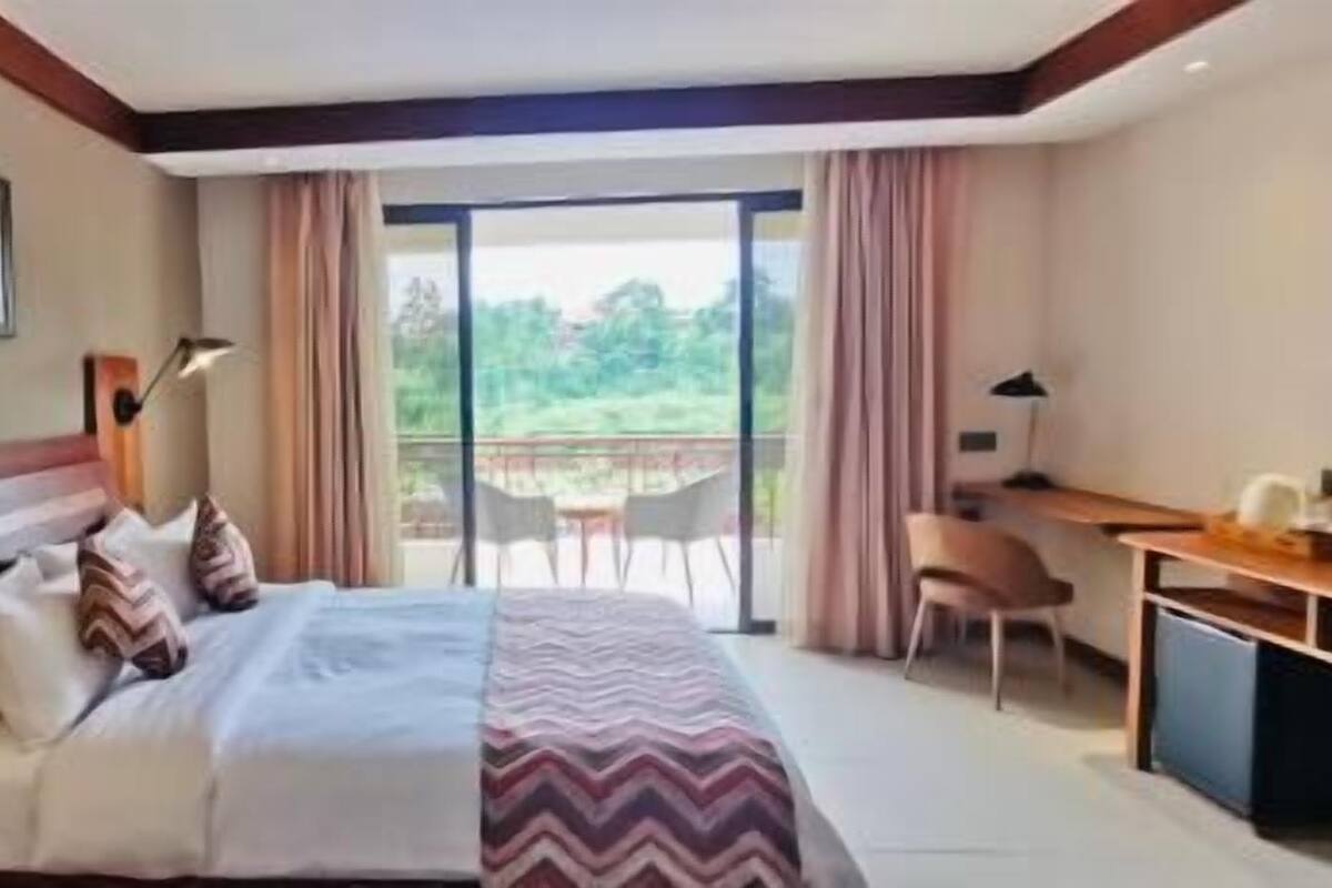 A hotel room with a bed, desk, and a balcony with a view.