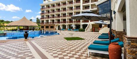 A hotel with a swimming pool, outdoor seating, and a building with multiple balconies.