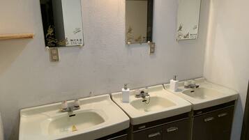 Une salle de bain avec trois lavabos, chacun étant surmonté d’un miroir. On trouve des placards sous les lavabos.