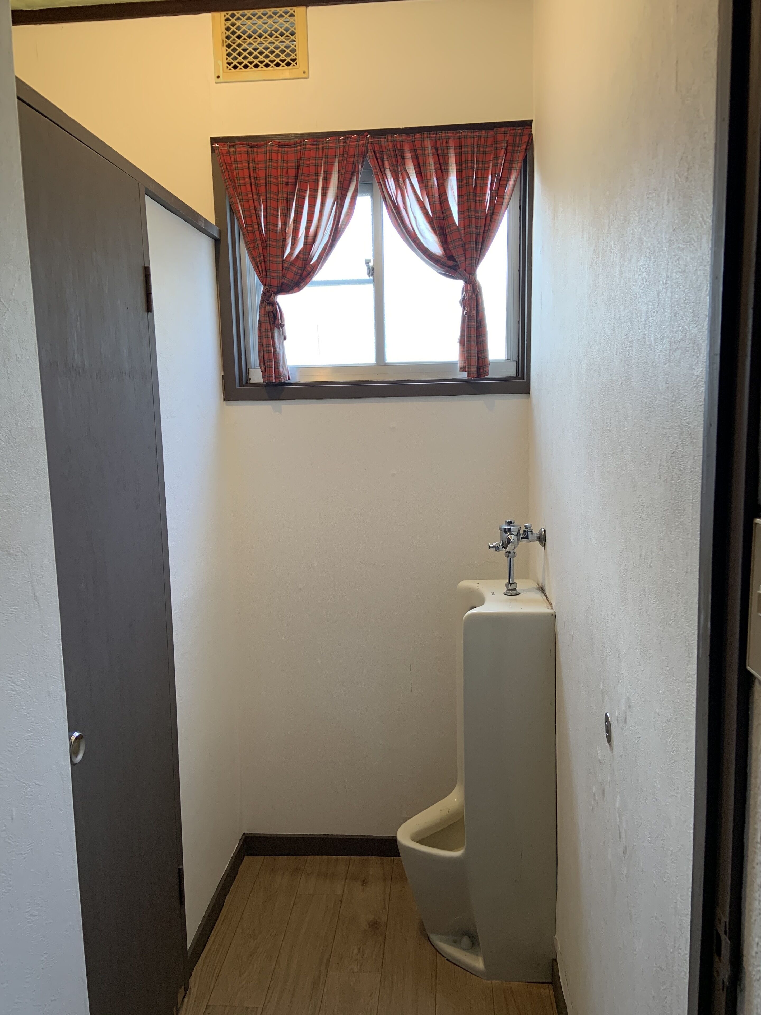 Un baño pequeño y estrecho con inodoro, una ventana con cortinas escocesas y un lavamanos.