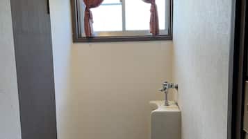 Un baño pequeño y estrecho con inodoro, una ventana con cortinas escocesas y un lavamanos.