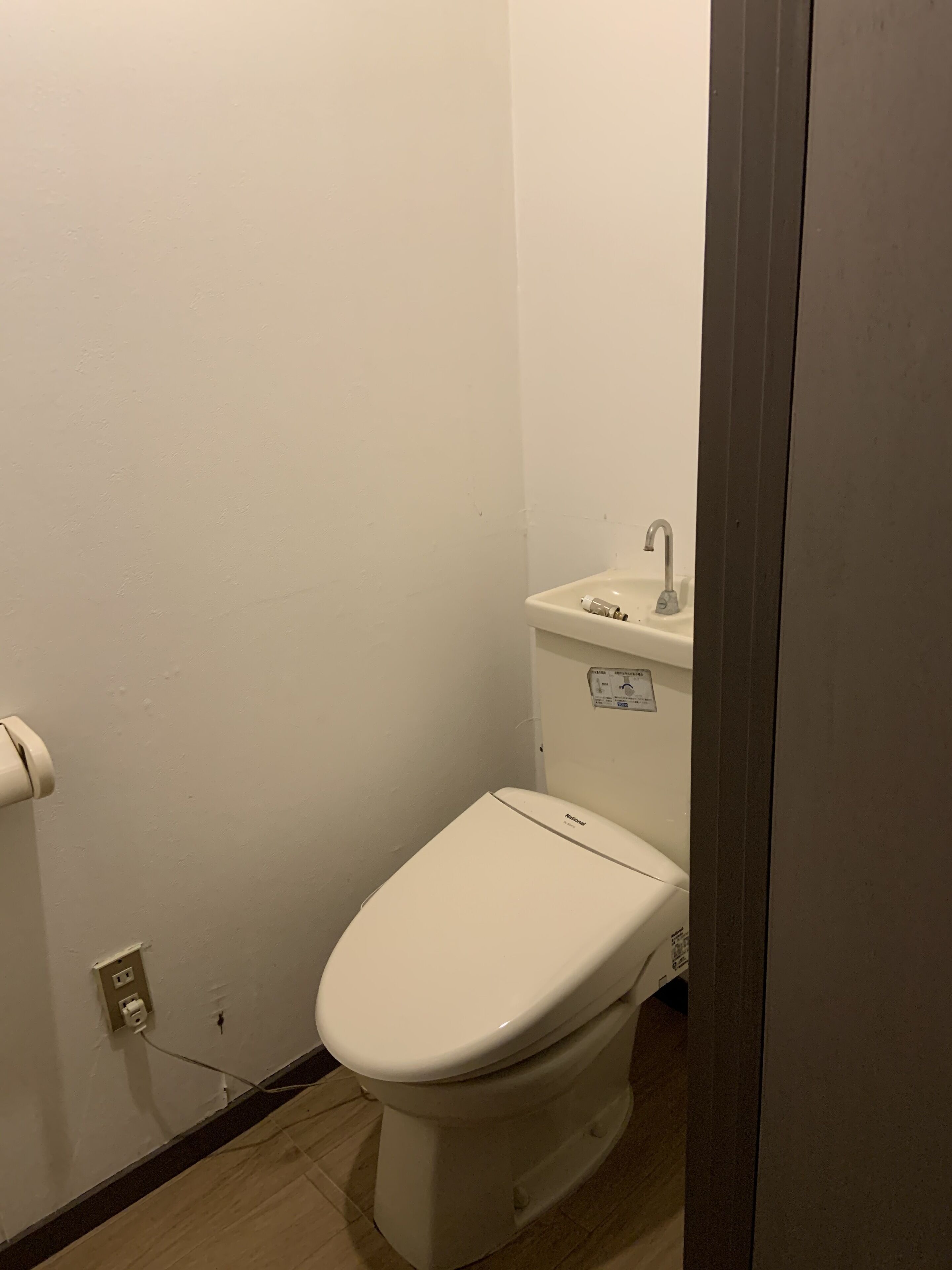 Un baño pequeño y blanco con inodoro, lavamanos y un porta papel higiénico en la pared.