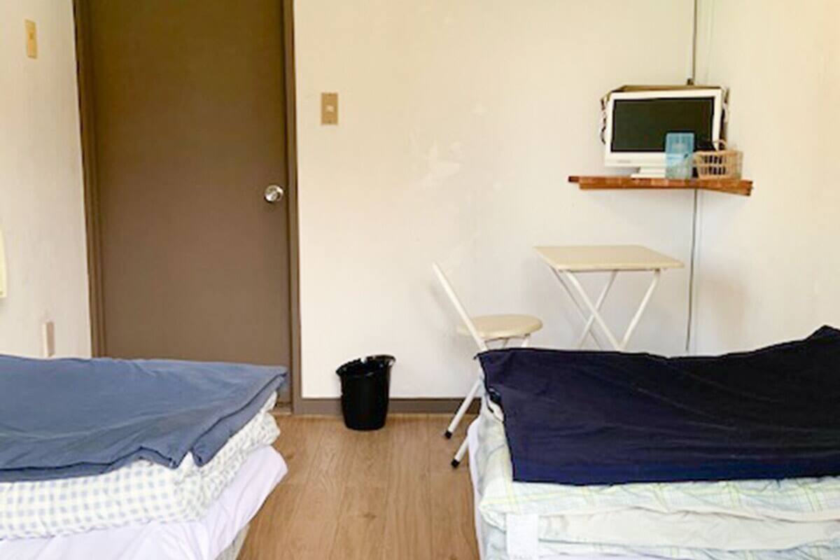A room with two beds, a desk, a chair, and a computer monitor on a shelf.