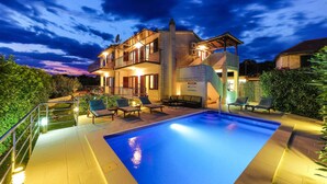 Una casa a due piani con piscina, area salotto esterna e un balcone.