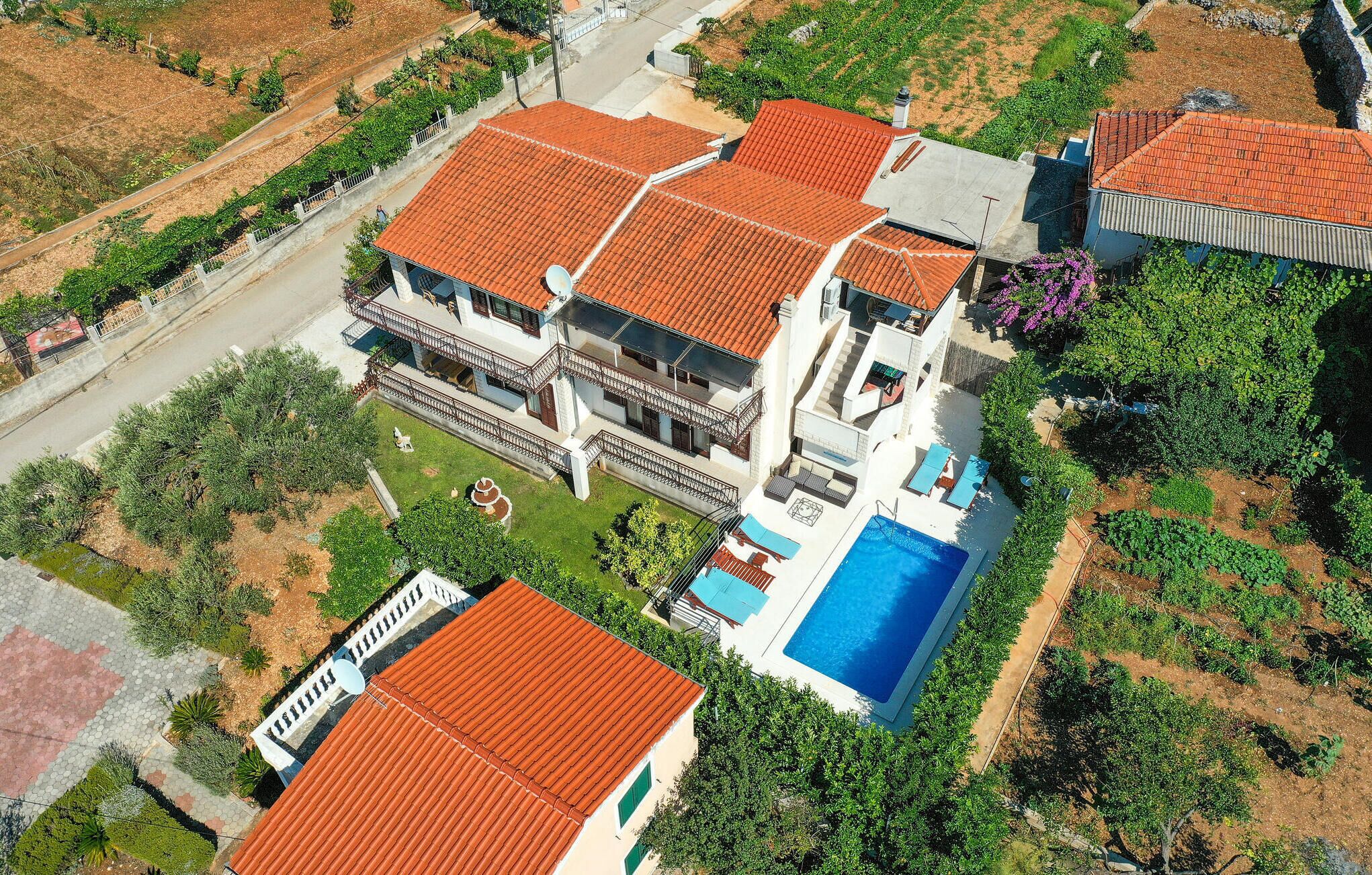 A large two-story house with a swimming pool, surrounded by greenery and a paved driveway.