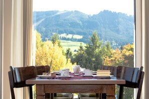 A dining table with chairs, a dessert plate, cups, and a book, set against a window with a view of a mountainous landscape. - Allgäuhaus Wertach (Wertach)