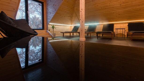 A spacious room with wooden walls and a sloped ceiling, featuring a large window, several chairs, and a small table. - Kozjanski dvor (Kozje)