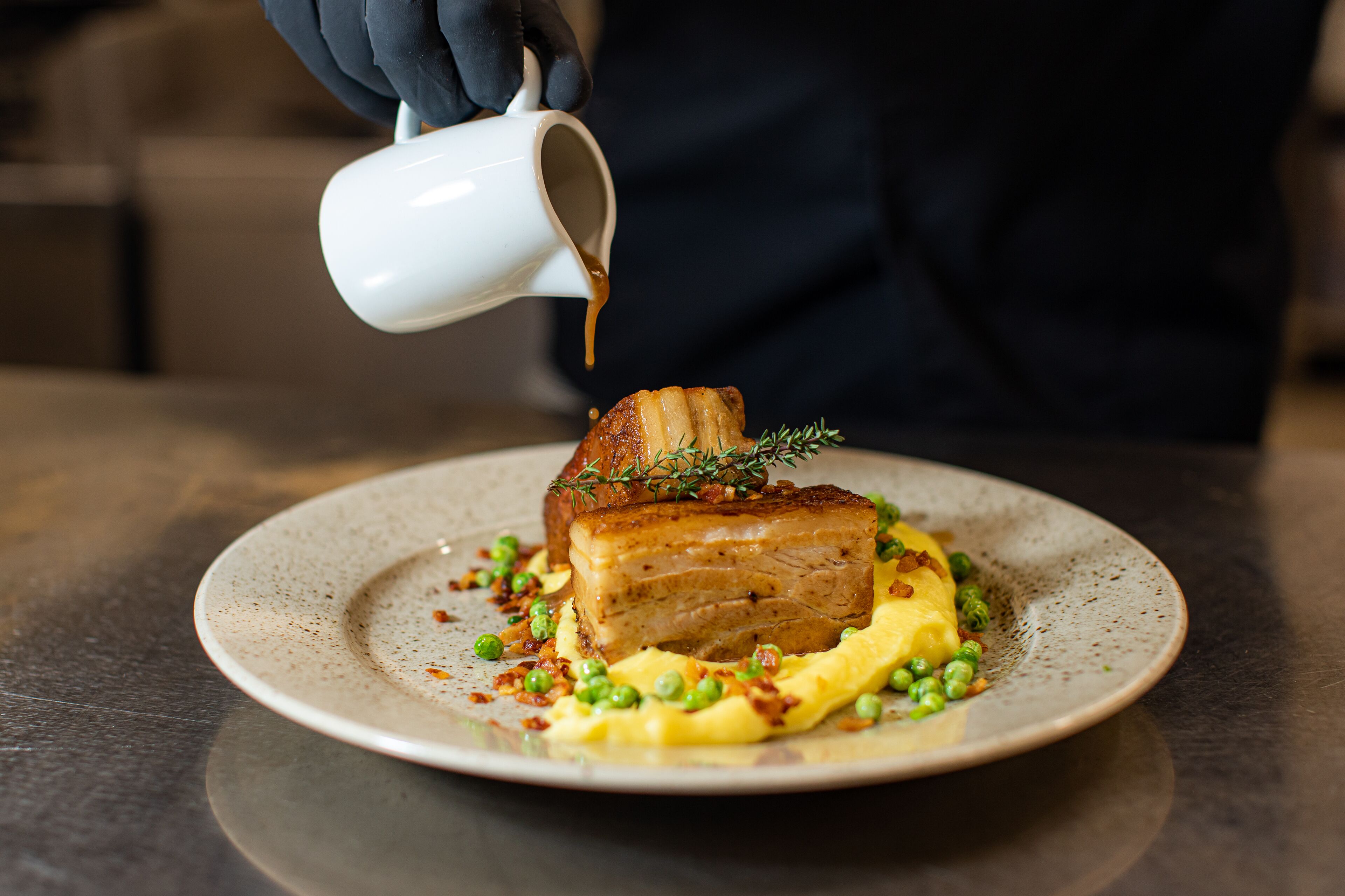 A chef pouring sauce over a dish on a plate.