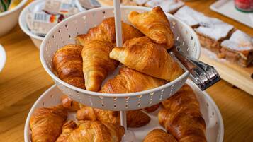 A table with a three-tiered stand holding croissants, a coffee pot, and a variety of other food items.