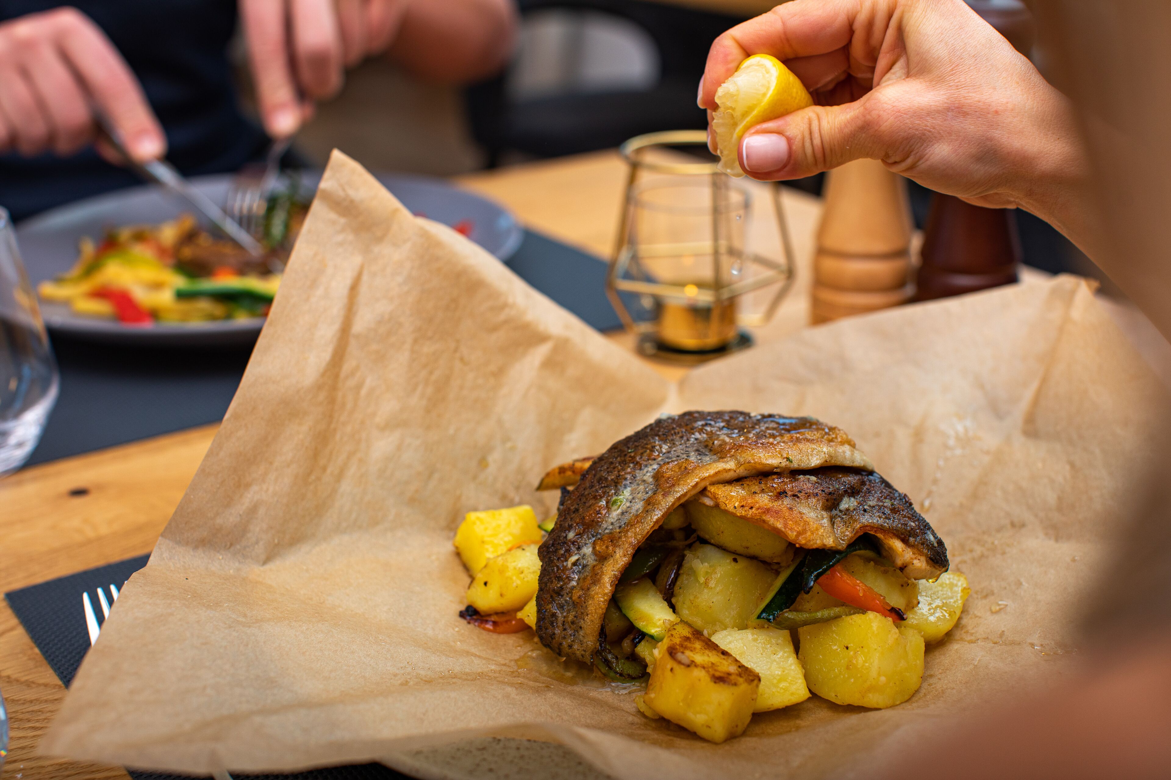 Un repas composé d’un sandwich emballé dans du papier, d’un verre d’eau et d’un moulin à poivre posés sur une table.