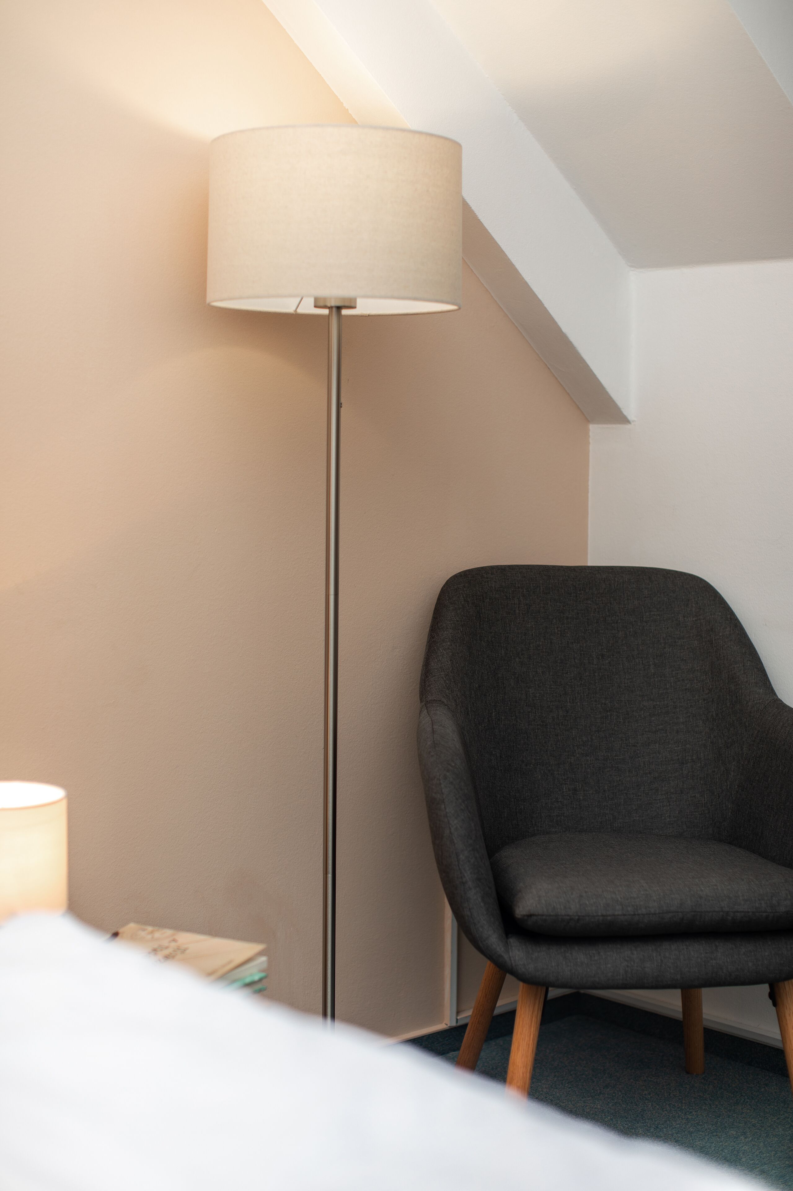 Una habitación con una lámpara de pie, un sillón gris oscuro y una cama.