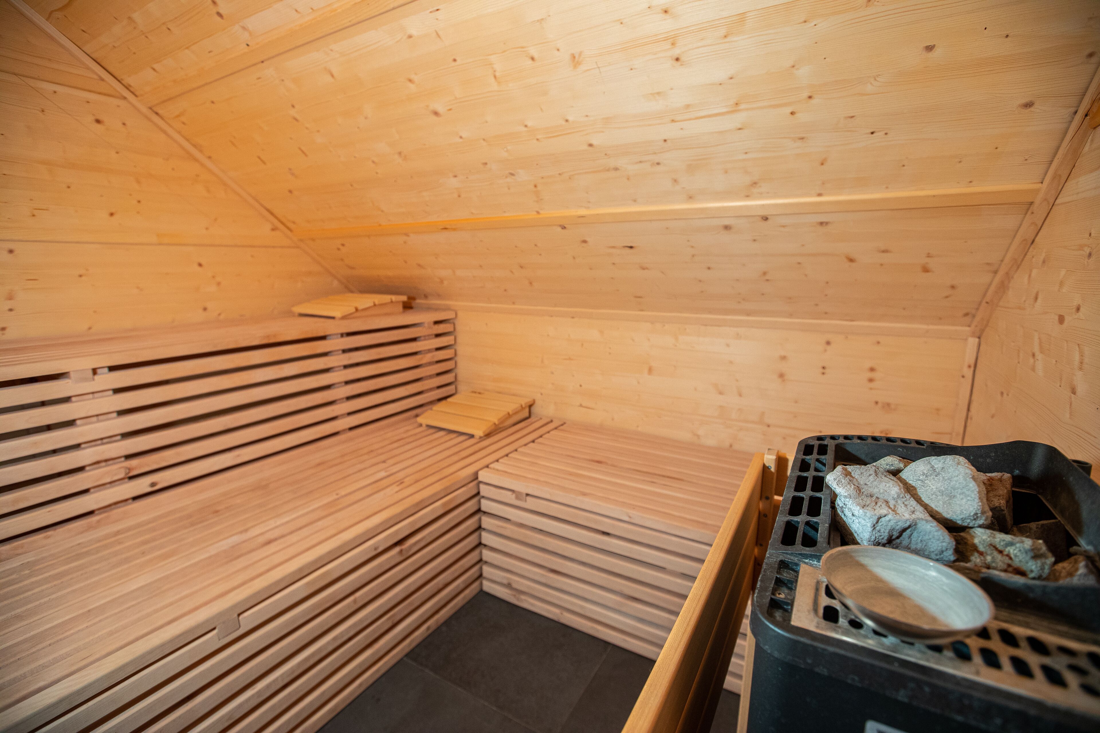 A sauna room with wooden benches and a black heating unit.