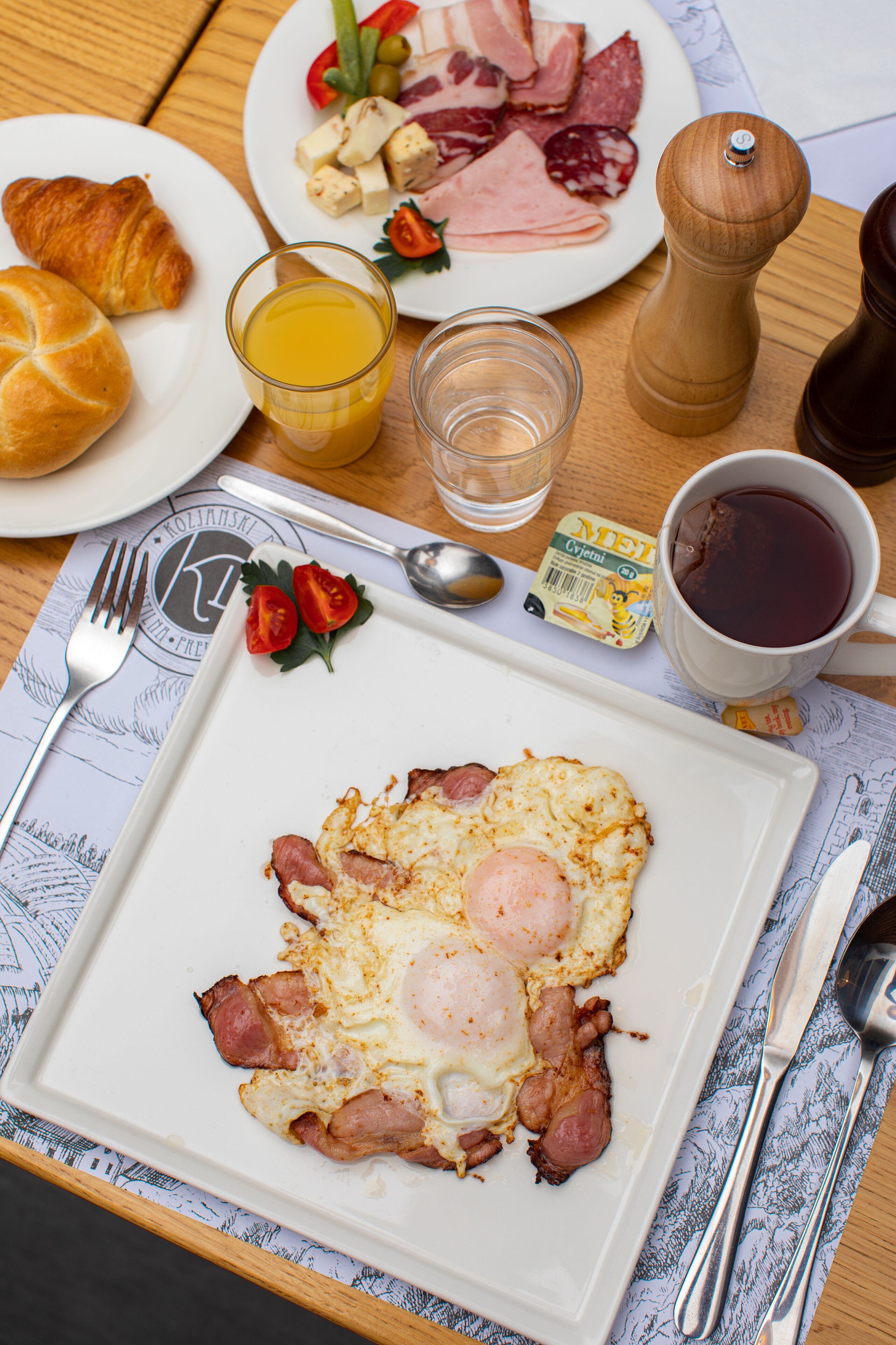 A breakfast plate with eggs, ham, and croissants, a glass of orange juice, and a cup of coffee on a wooden table.