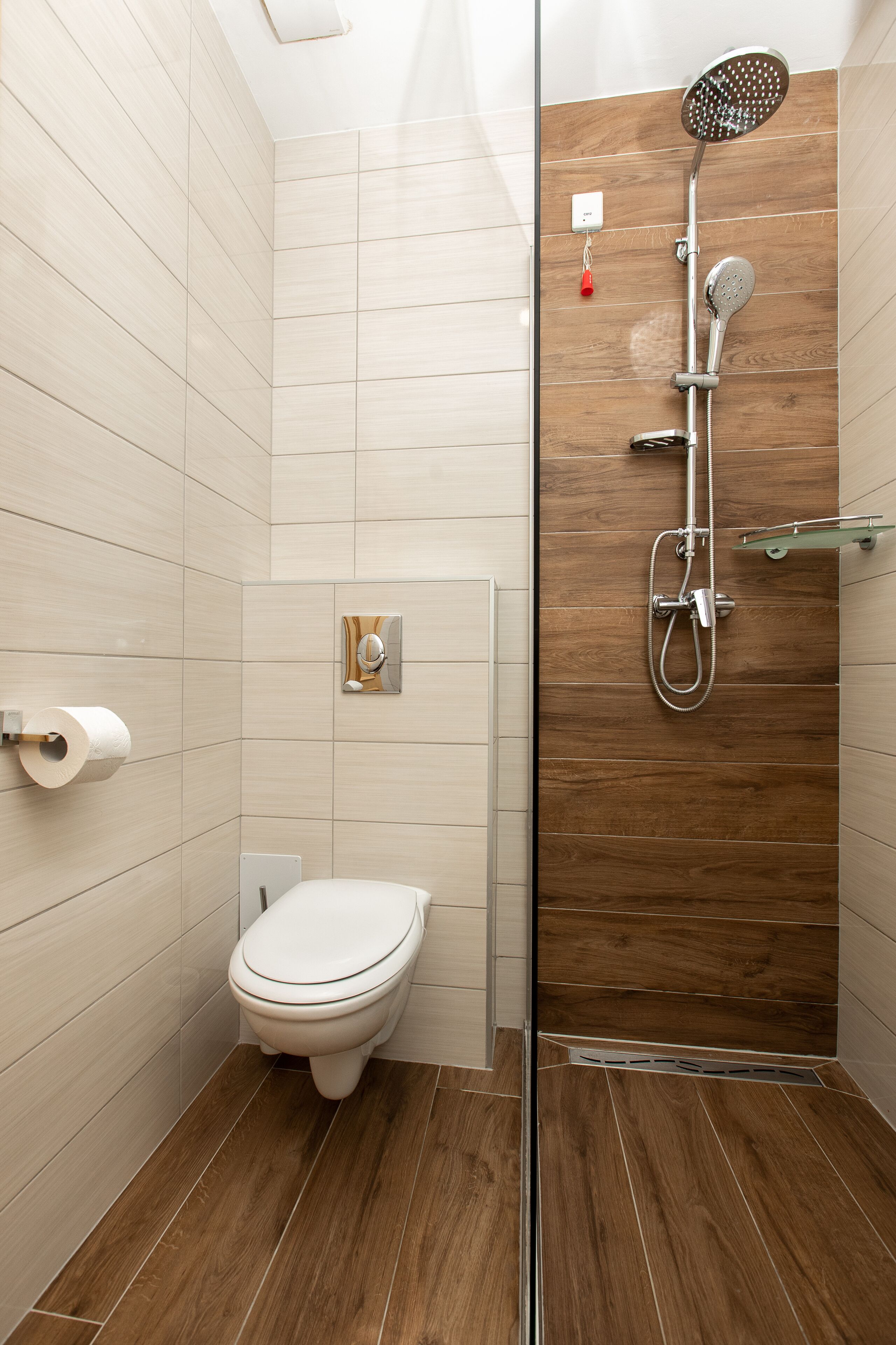 A bathroom with a toilet, a shower with a glass door, and a wooden floor.