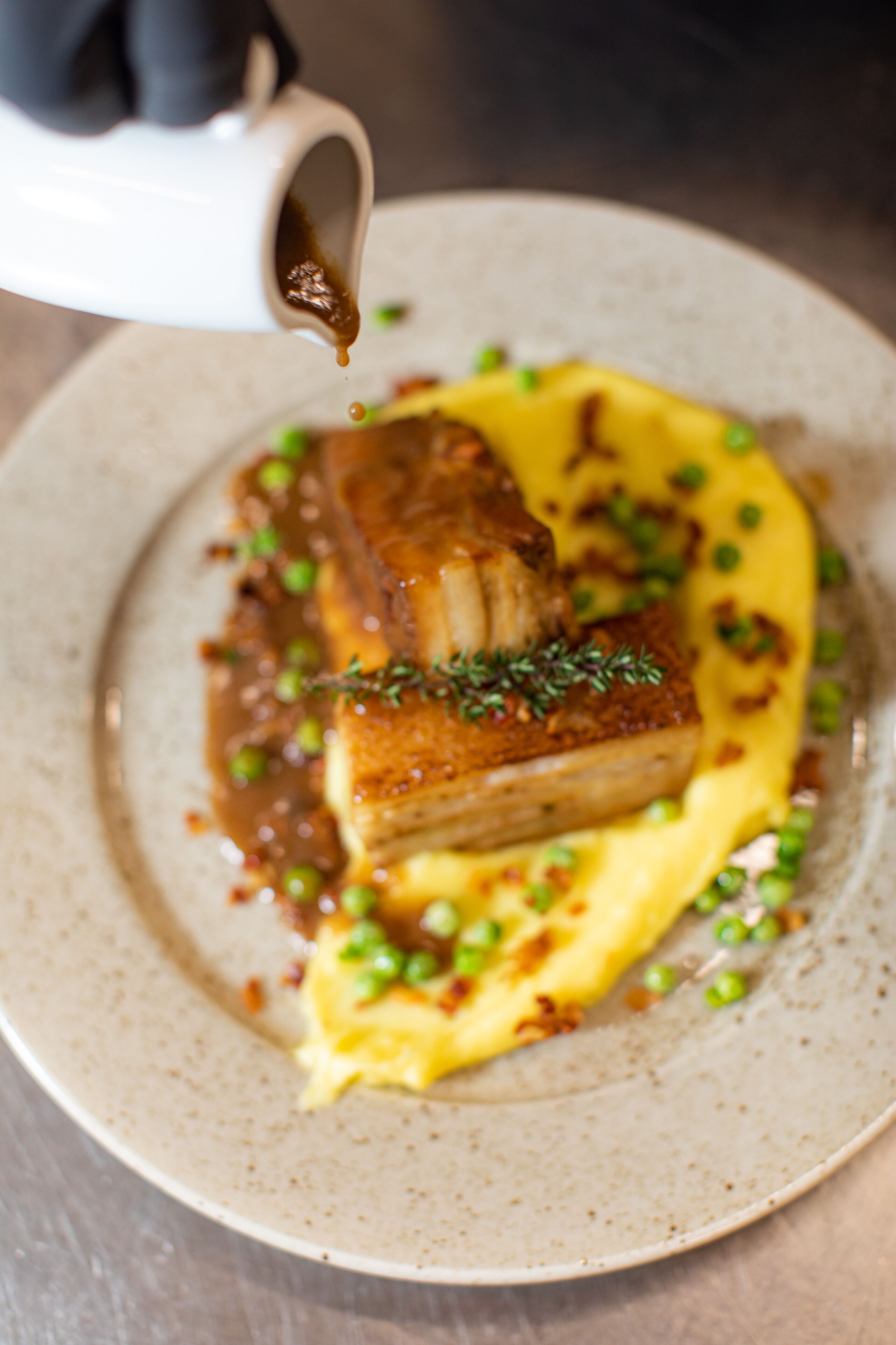 A plate with a piece of meat, peas, and sauce.
