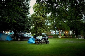 A camping area with a tent, a motorcycle, and a car parked nearby.