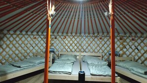 A traditional yurt with four beds arranged in a circular pattern, wooden lattice walls, and a central light fixture. - Haller Wooden Houses - Campsite (Budapest)