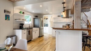 Una cocina moderna con armarios blancos, techo de madera y comedor con mesa y sillas blancas.
