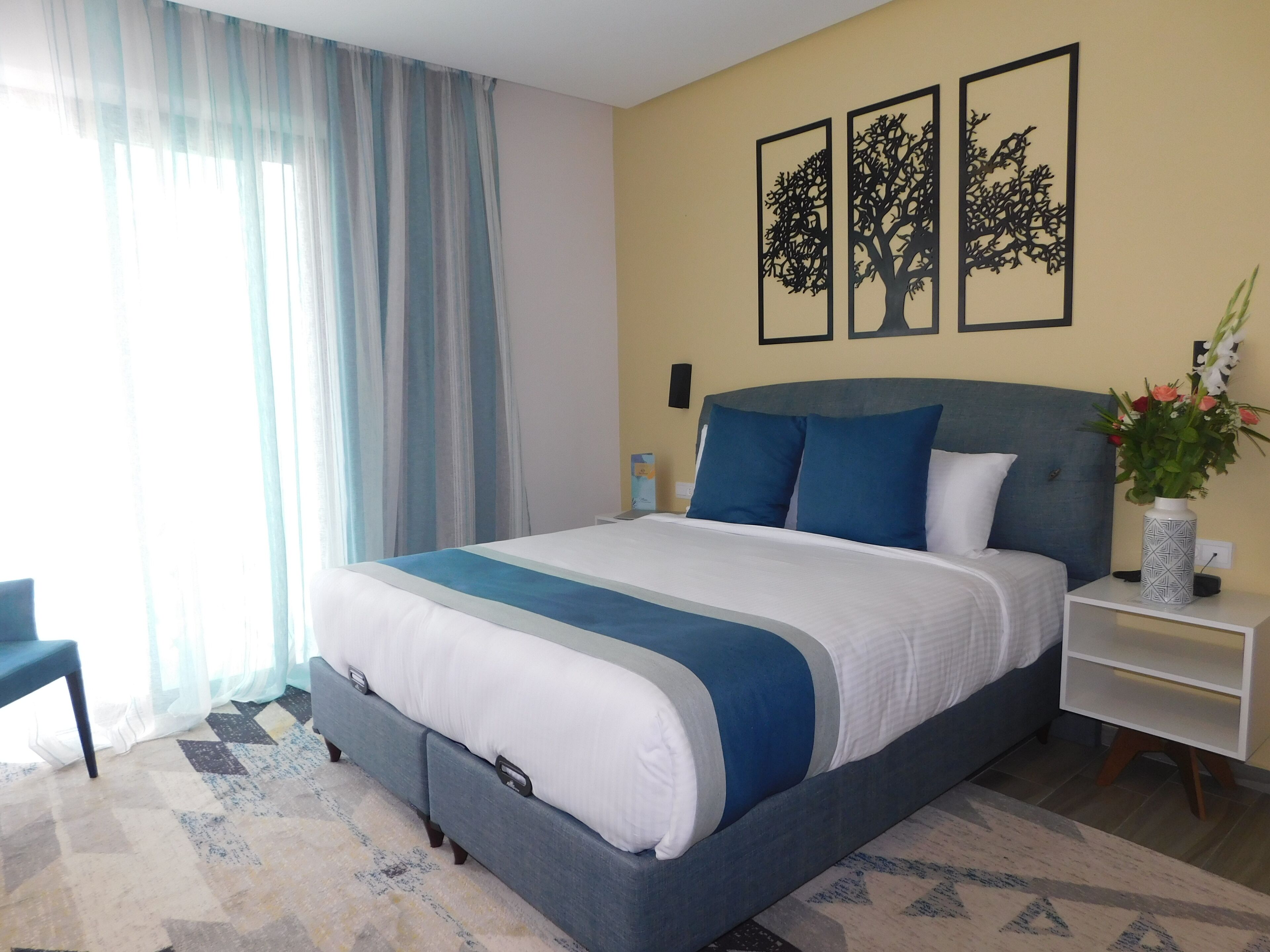 Quarto bem arrumado com uma cama grande, uma mesinha de cabeceira com um vaso de flores e uma cadeira.