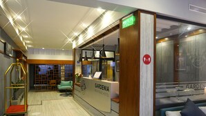 Un espace d’accueil d’hôtel comprenant un comptoir de réception, un coin salon avec un canapé et des fauteuils, un escalier et une plante décorative.