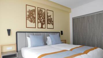 Un letto matrimoniale con testiera grigia, due comodini e un tavolino da notte. Tre opere d'arte a parete raffigurano alberi.