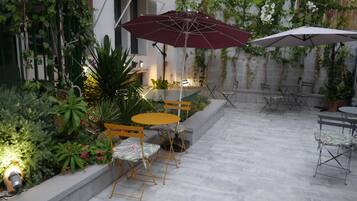 An outdoor patio area with a seating arrangement, including a table and chairs, surrounded by potted plants and a decorative wall.