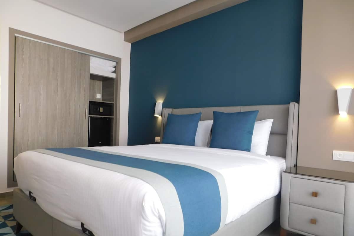 Une chambre d’hôtel avec un grand lit, une table de chevet, une armoire et une salle de bain visible à travers une porte ouverte.