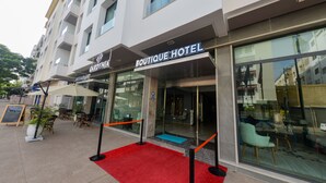 L’entrée d’un hôtel-boutique avec un tapis rouge, des sièges en plein air et une enseigne indiquant la présence d’un restaurant.