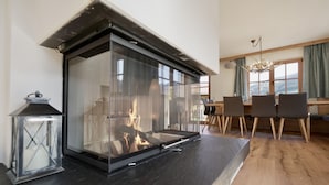 Una sala de estar moderna con chimenea de vidrio, piso de madera, un comedor con sillas y vistas al exterior a través de amplias ventanas.
