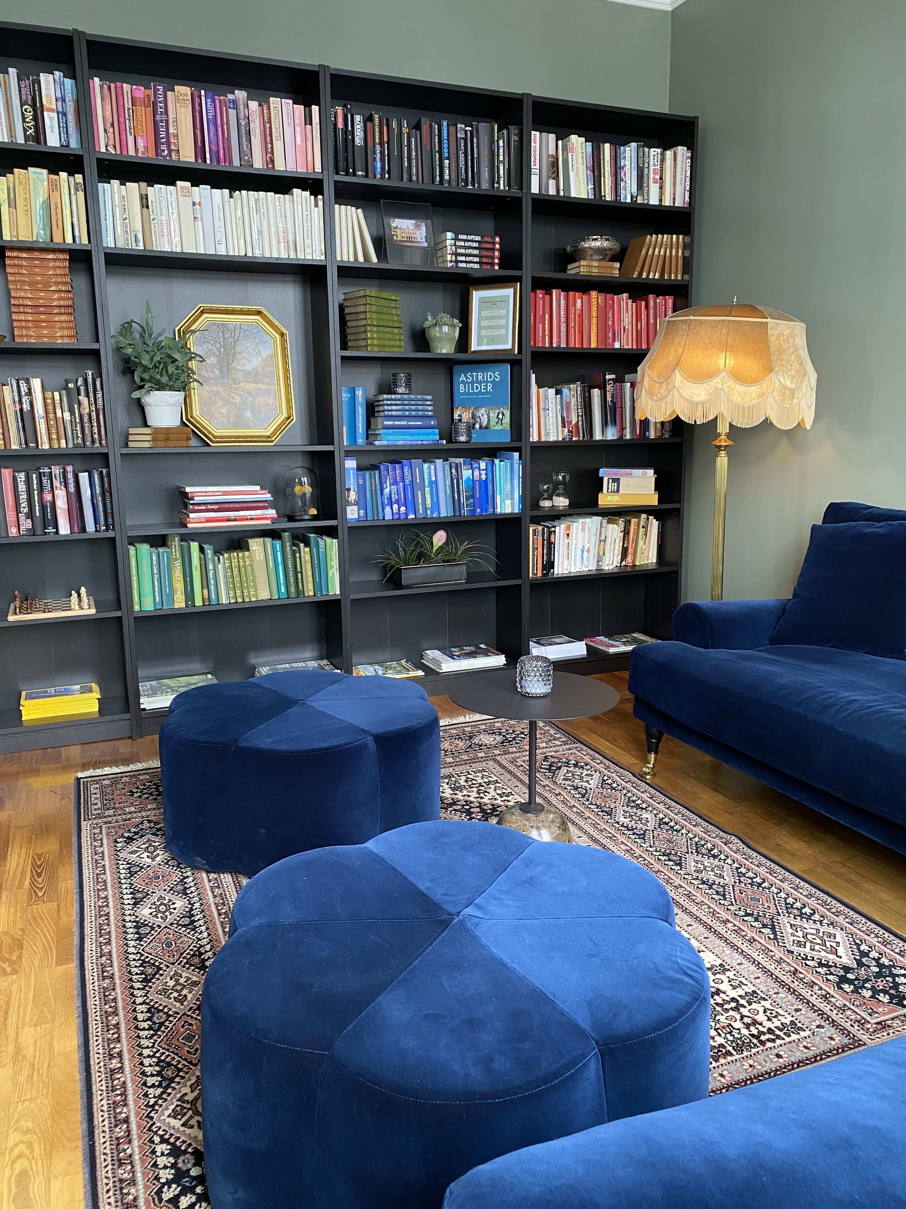 A living room with a large bookshelf, blue ottomans, a blue sofa, and a patterned rug.
