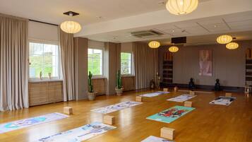 A spacious room with wooden flooring, large windows with curtains, and several exercise mats laid out.