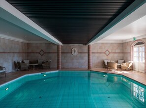 A large indoor swimming pool with tiled walls and ceiling, surrounded by lounge chairs and a small table. - Johannesbergs Slott (Rimbo)