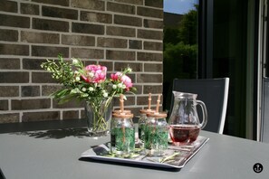 Une table avec un pichet en verre, un vase rempli de fleurs roses et trois bocaux en verre contenant des feuilles vertes.