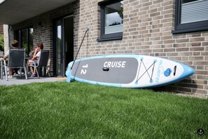 Une planche de paddle marquée du mot « CRUISE » est appuyée contre un bâtiment en briques.