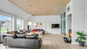Una sala de estar moderna con techo de madera, ventanas amplias, chimenea y televisor.