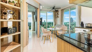 A modern kitchen with a glass island, dining area with chairs, and a view of the city. - Panoramic Sea, City And Mountain Views by City Garden Tower (Pattaya)