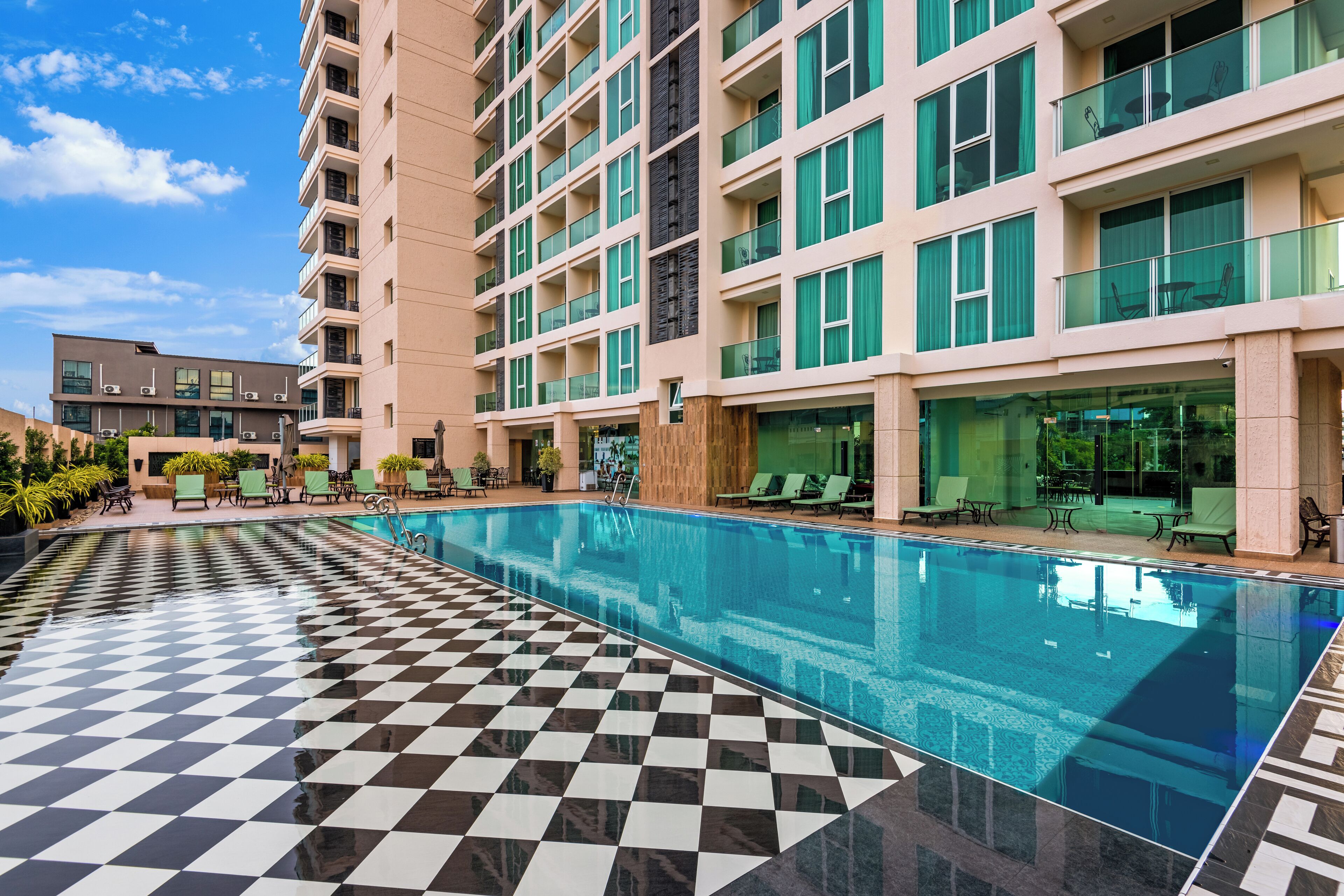 A modern hotel with a large indoor pool, checkered floor, and outdoor seating area.
