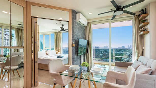 A modern living room with a glass dining table, two armchairs, a sofa, and a ceiling fan. - Panoramic Sea, City And Mountain Views by City Garden Tower (Pattaya)