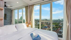A large bed with white linens and rolled towels, a ceiling fan, and a city view through large windows. - Panoramic Sea, City And Mountain Views by City Garden Tower (Pattaya)
