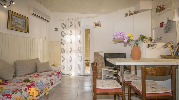 Un salon confortable avec un canapé, une table à manger et des chaises, un téléviseur et un coin cuisine équipé d’une cuisinière.