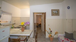 Une cuisine compacte comprenant une table et des chaises, un réfrigérateur et un évier. La pièce adjacente contient un lit recouvert d’une couvre-lit à motifs floraux.