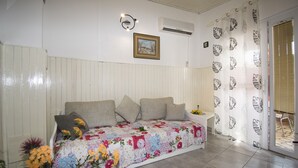 Une chambre comprenant un lit, une table de chevet, un climatiseur fixé au mur, un tableau encadré et une fenêtre avec des stores.