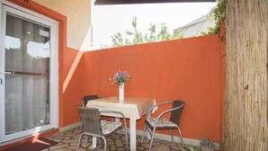 Une terrasse avec une table et des chaises, un pot de fleurs et une clôture en bambou.