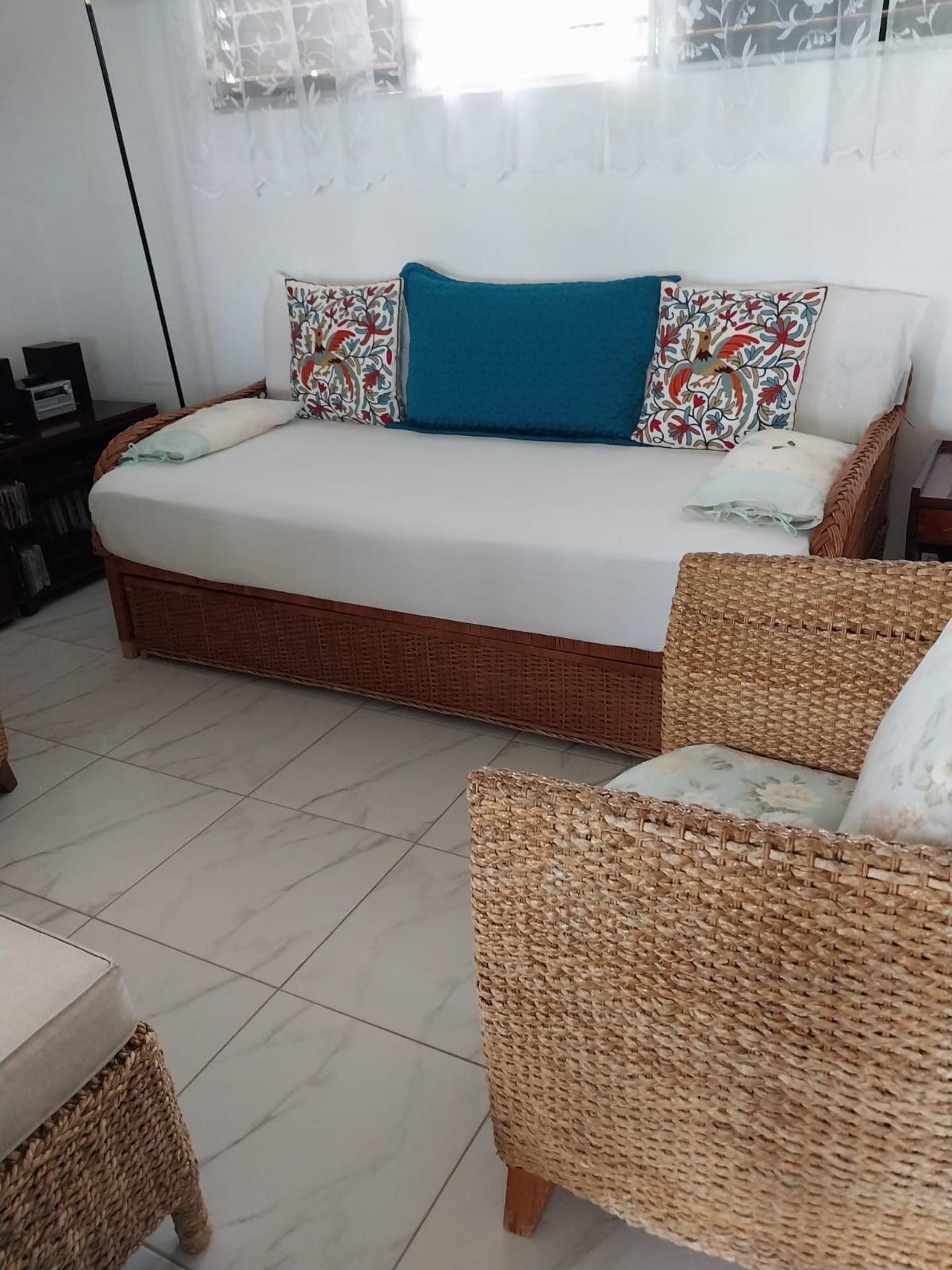 Un letto con un cuscino blu, cuscini decorati e una sedia in vimini con un cuscino floreale.