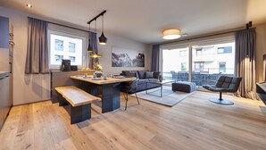 Un salon moderne avec un plancher en bois, un canapé, une table basse, un coin repas avec un banc et une grande fenêtre avec des rideaux.